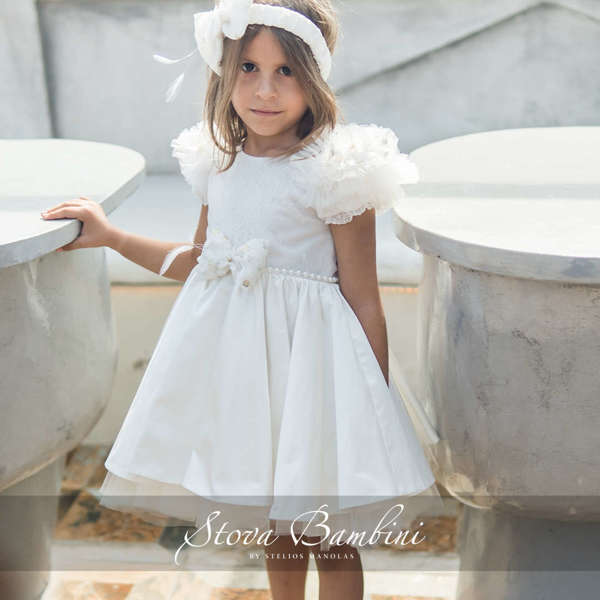 Εντυπωσιακό, χειροποίητο off white φόρεμα με τα χαρακτηριστικά τούλινα μανίκια Stova Bambini. To κορσάζ είναι διακοσμημένο με δαντέλα και έχει συνδυαστεί με εντυπωσιακό φιόγκο και ζώνη από πέρλες. 